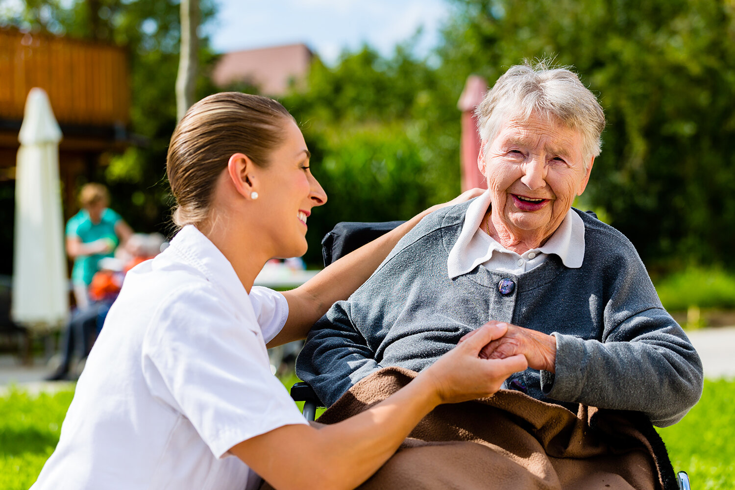 Caregiver sitting beside an older woman outdoors and talking with her warmly