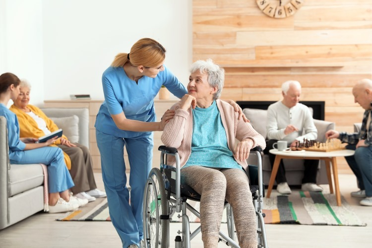 Caregiver supporting an older woman in a wheelchair inside a senior living community