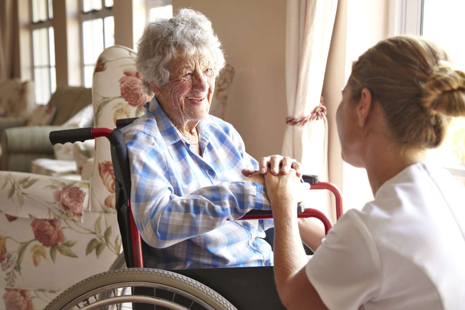 Caregiver holding hands with an older woman in a wheelchair during a calm conversation