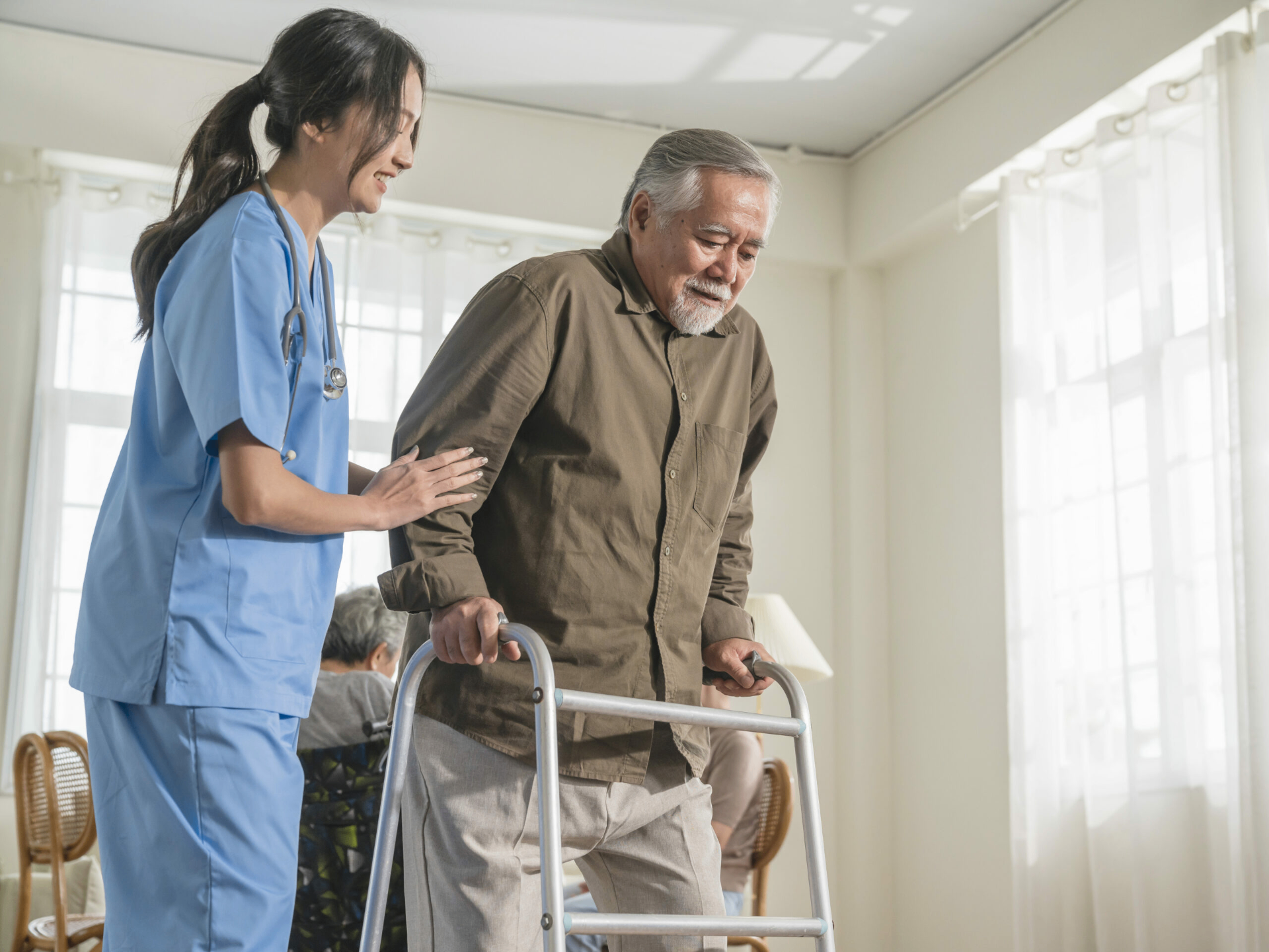 Caregiver helping an older man walk safely with a walker indoors