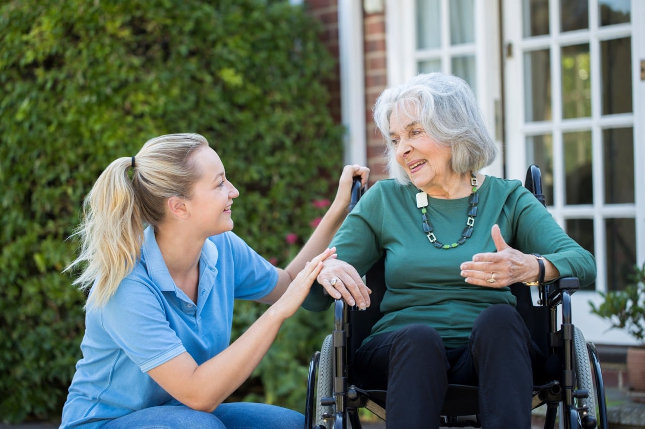 Caregiver talking with an older woman in a wheelchair outside a home